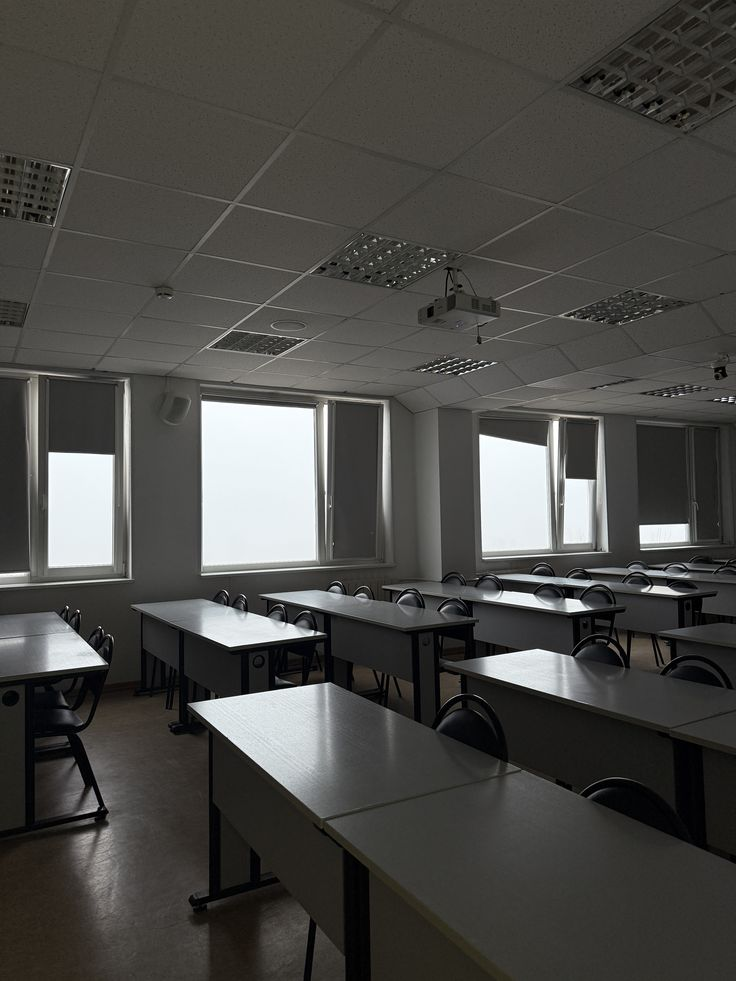 An empty classroom with rows of desks and pale window light.