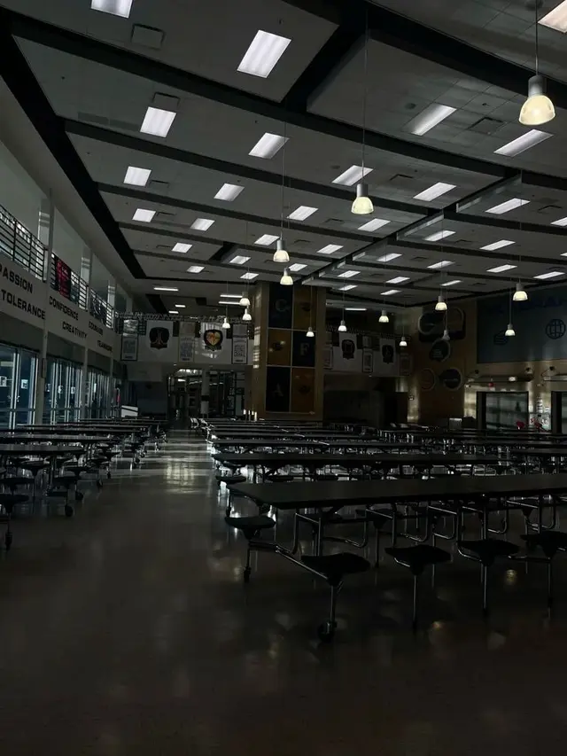 An empty institutional dining hall beneath a geometric ceiling.
