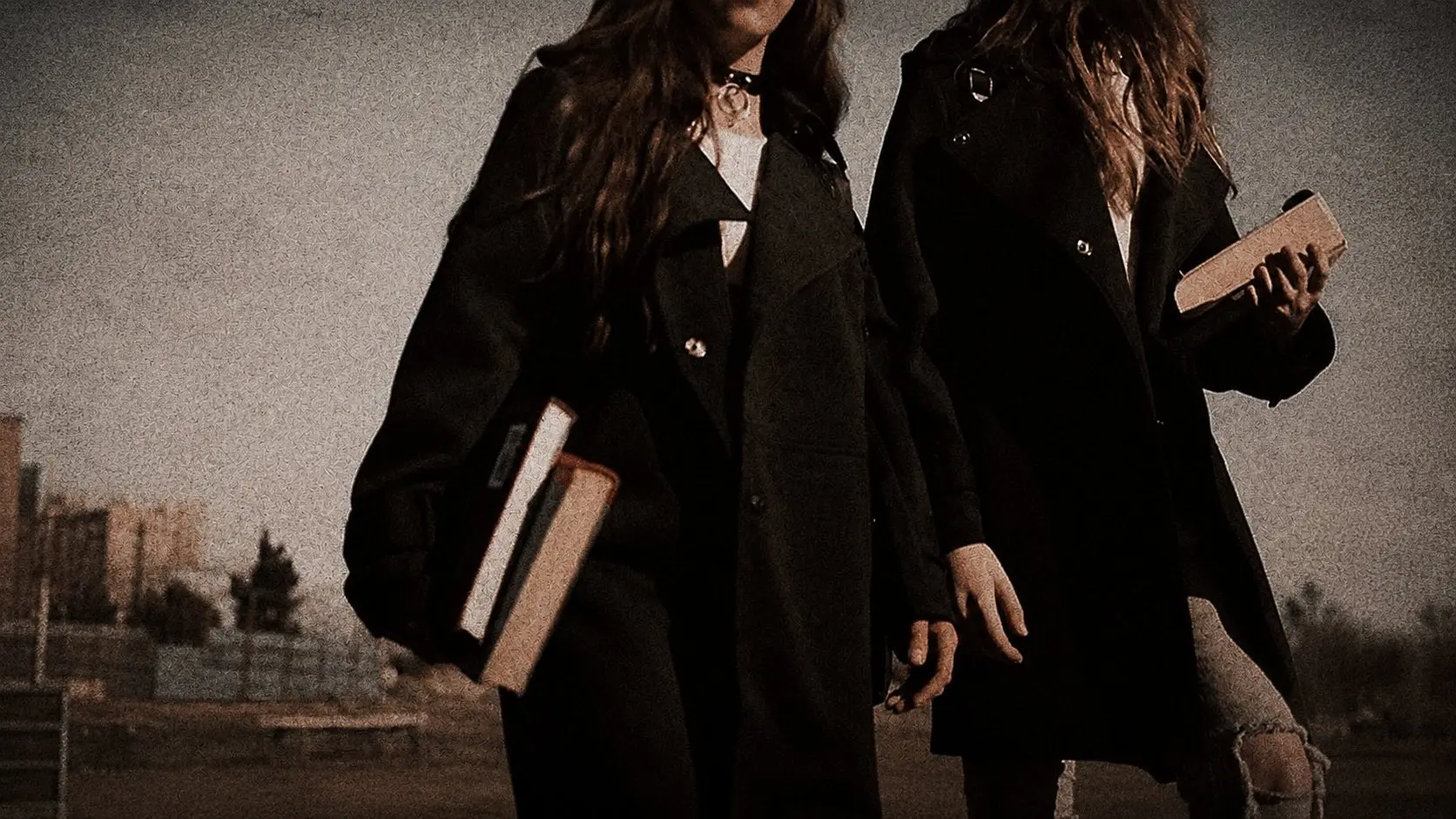 Two students in dark academic dress carrying books outdoors.