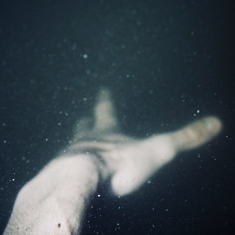 A blurred hand reaching toward another figure through dark glass.