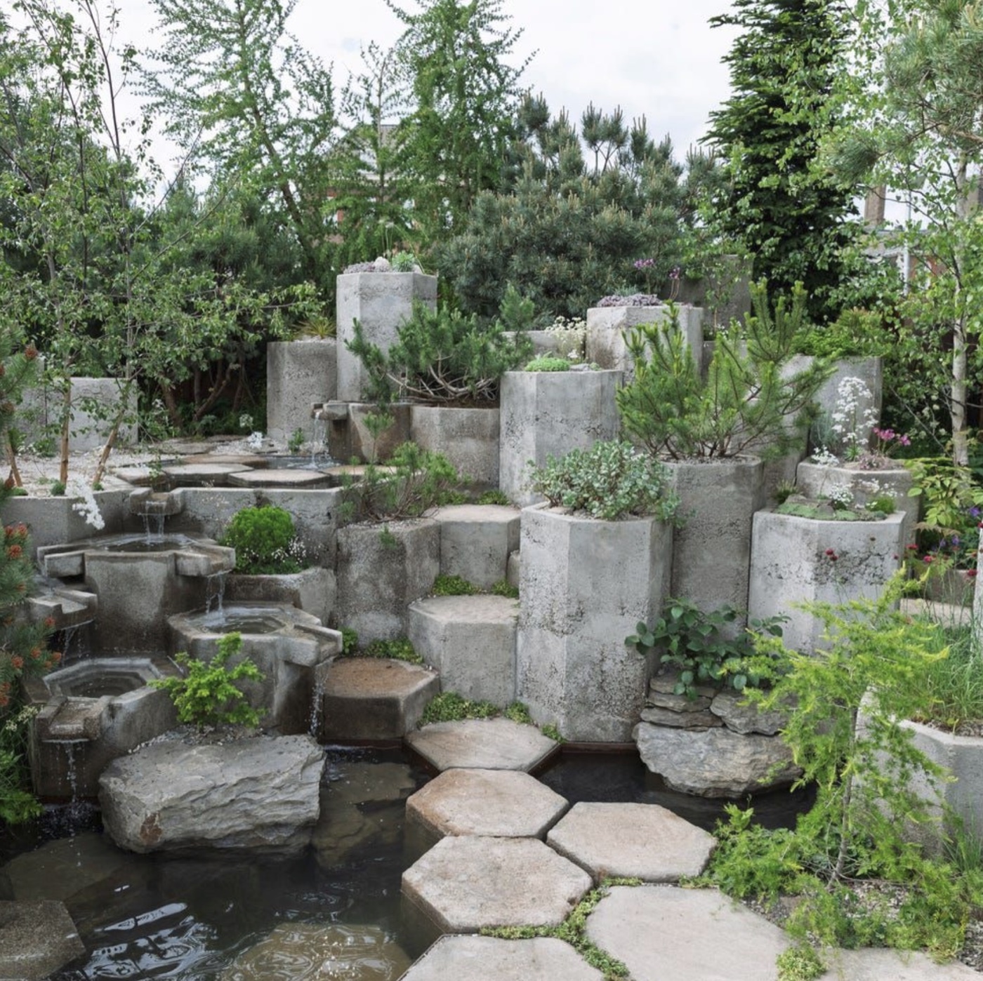 A regenerative concrete garden filled with trees, plants, water channels, and stepping stones.